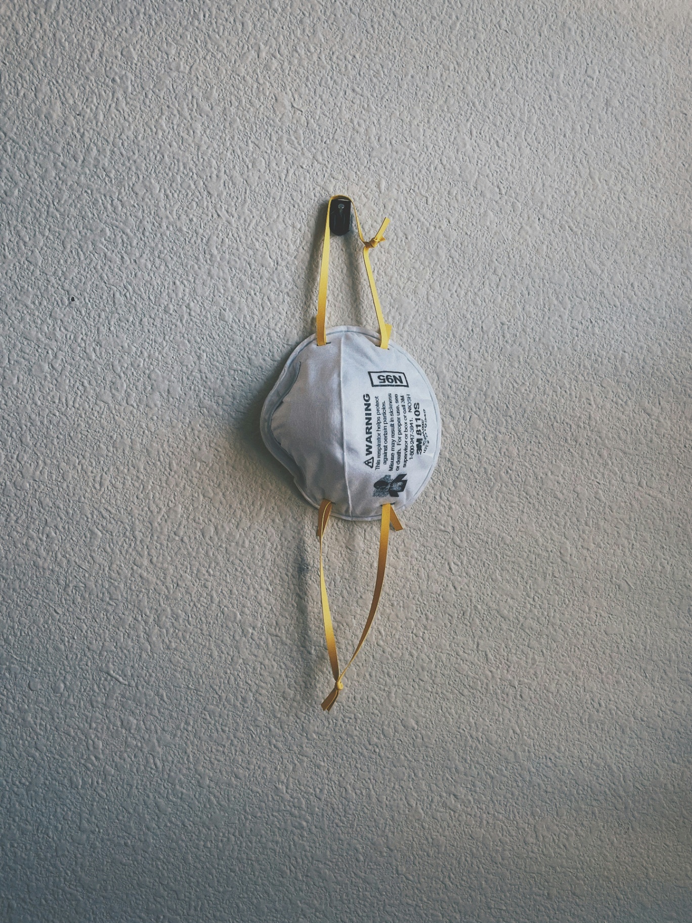 An N95 respirator hanging on a textured wall, staged before a Pensacola crawlspace mold inspection